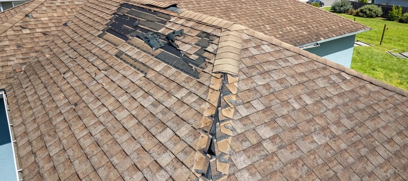 Residential asphalt shingle roof with damaged sections being prepared for replacement