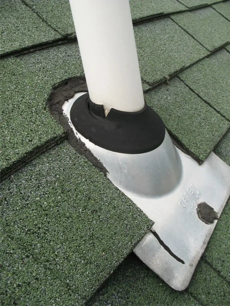 Split rubber pipe boot and sealant-patched vent flashing on an aged asphalt shingle roof before roof repair