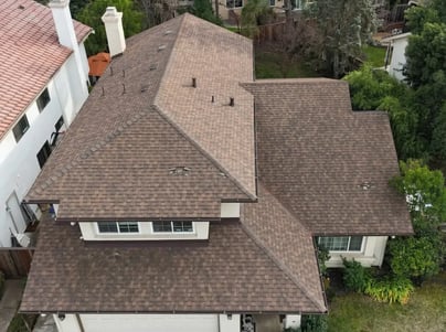 Aerial view of a complex hip roof with brown architectural shingles, ridge caps and vent pipes after a re-roof