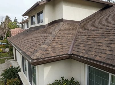 Brown architectural asphalt shingles and matching gutters after roof replacement on a two-story stucco home