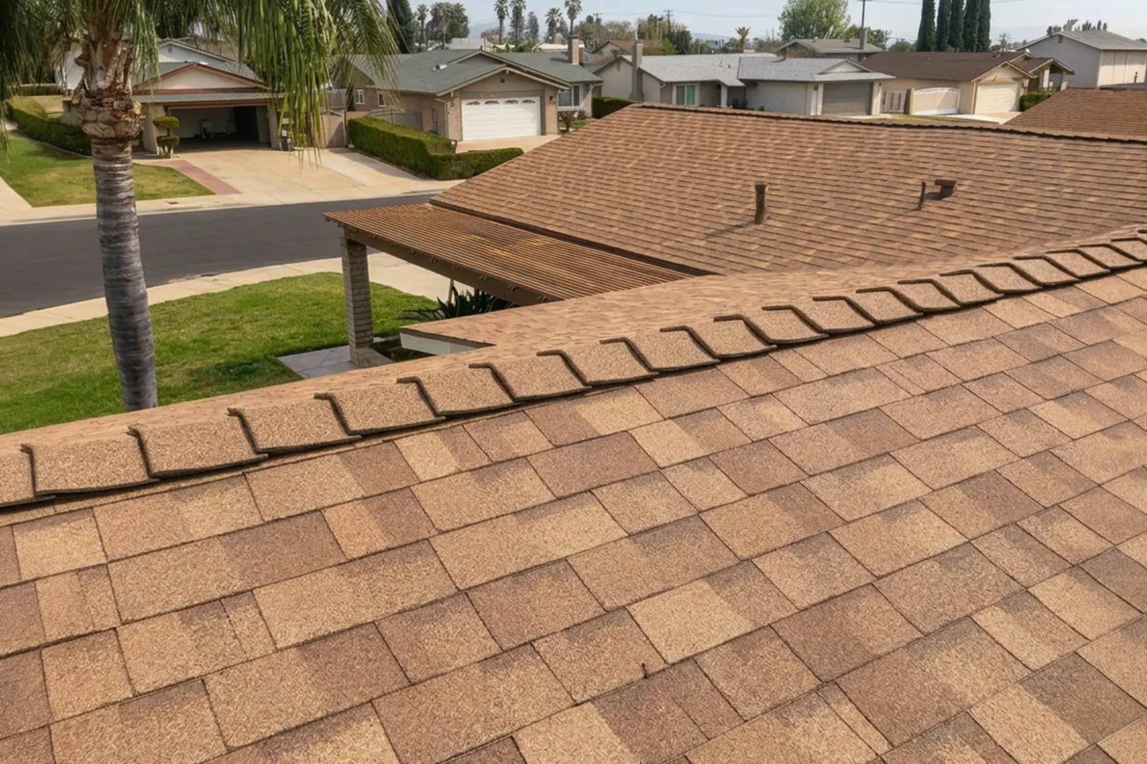 Newly installed brown asphalt shingle roof with ridge caps above a residential neighborhood, by Hybrid Renovations