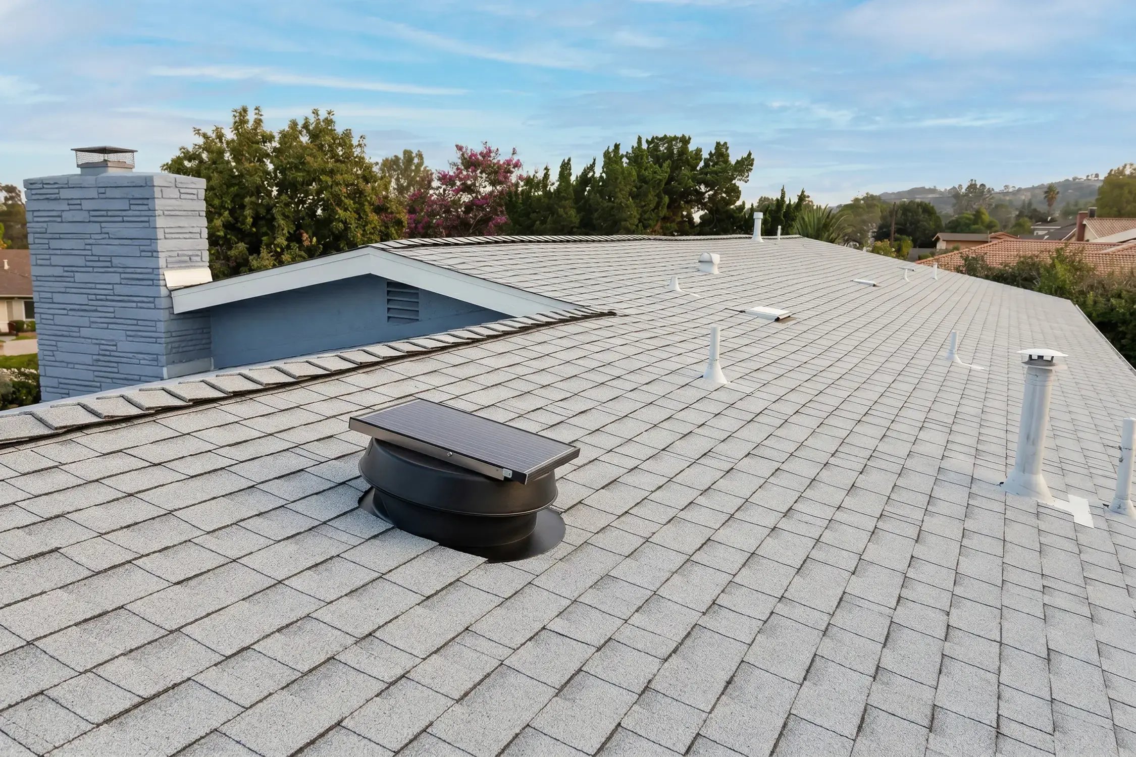 New cool-rated shingle roof with black solar attic fan and stone chimney after Hybrid Renovations re-roof, Duarte