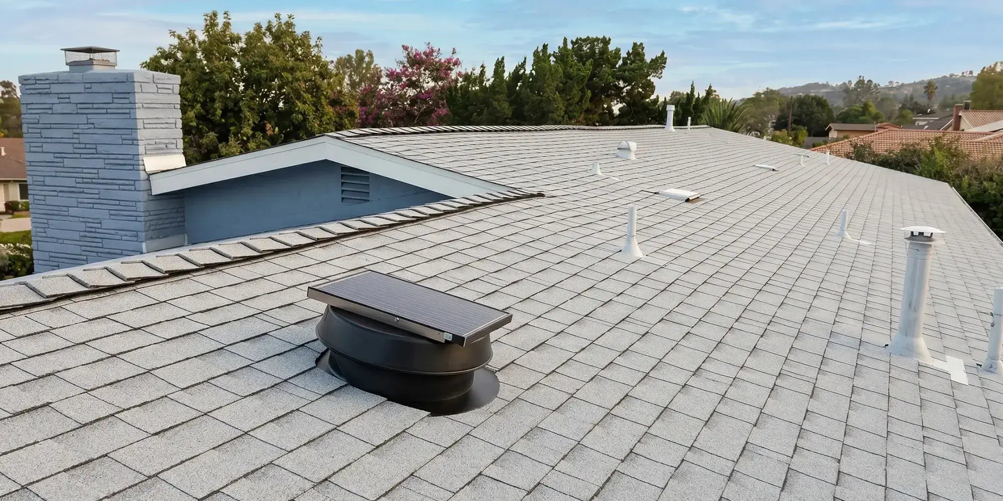 New cool-rated shingle roof with black solar attic fan and stone chimney after Hybrid Renovations re-roof, Duarte