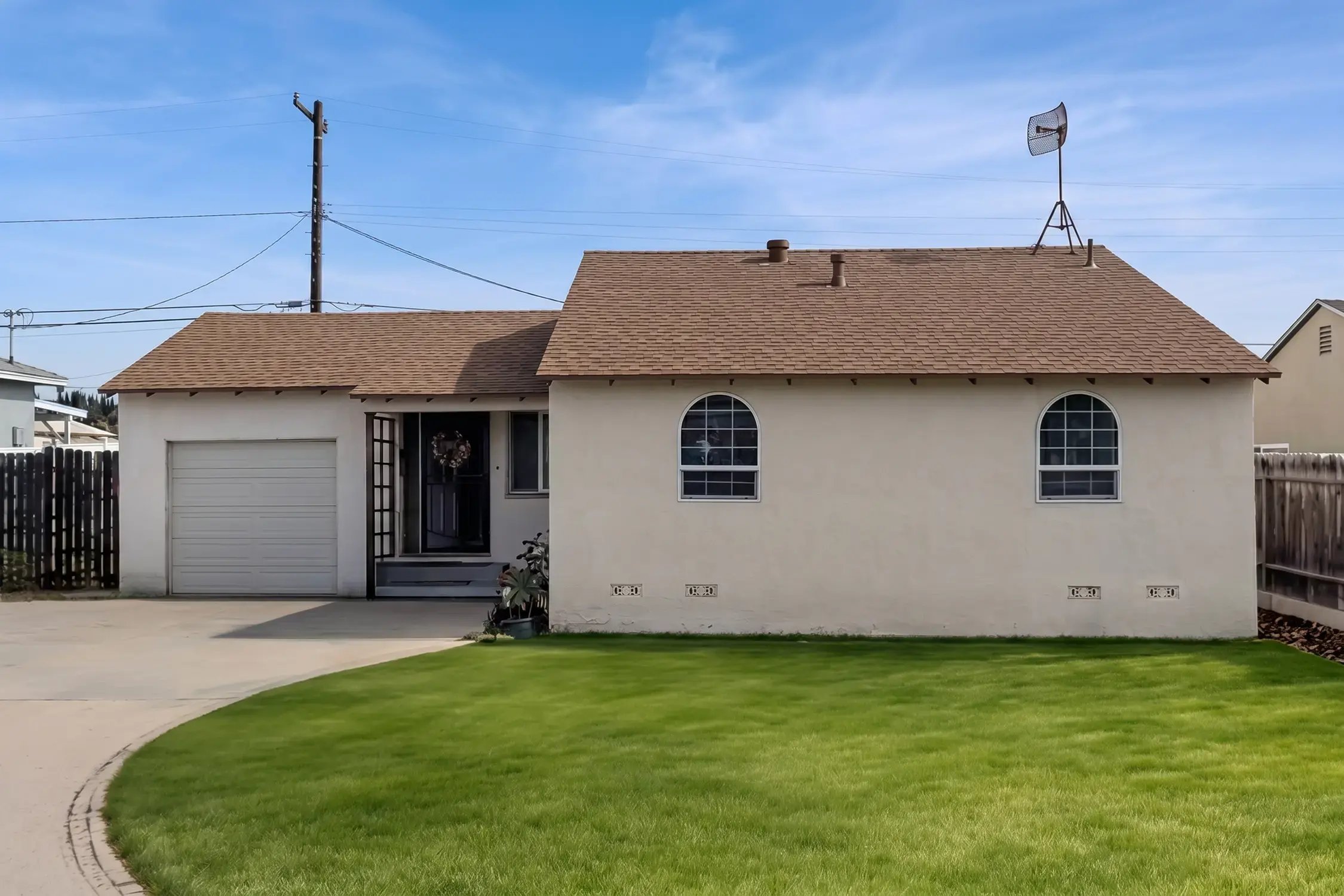 Front exterior of the single-story stucco home with its new brown roof and green lawn by Hybrid Renovations, La Habra