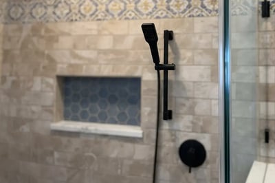 Matte black hand shower slide bar and valve trim beside a frameless glass panel after a shower rebuild