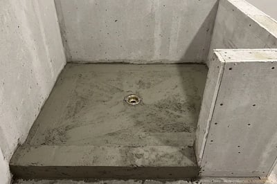 Dry-pack mortar bed sloped toward the center drain before waterproofing on a shower rebuild