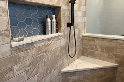 Blue hexagon tiled niche with a marble sill and a corner bench after a shower rebuild