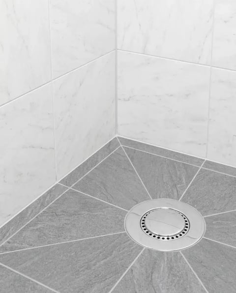 Sloped tile shower floor with grout lines converging on a square center drain after installation