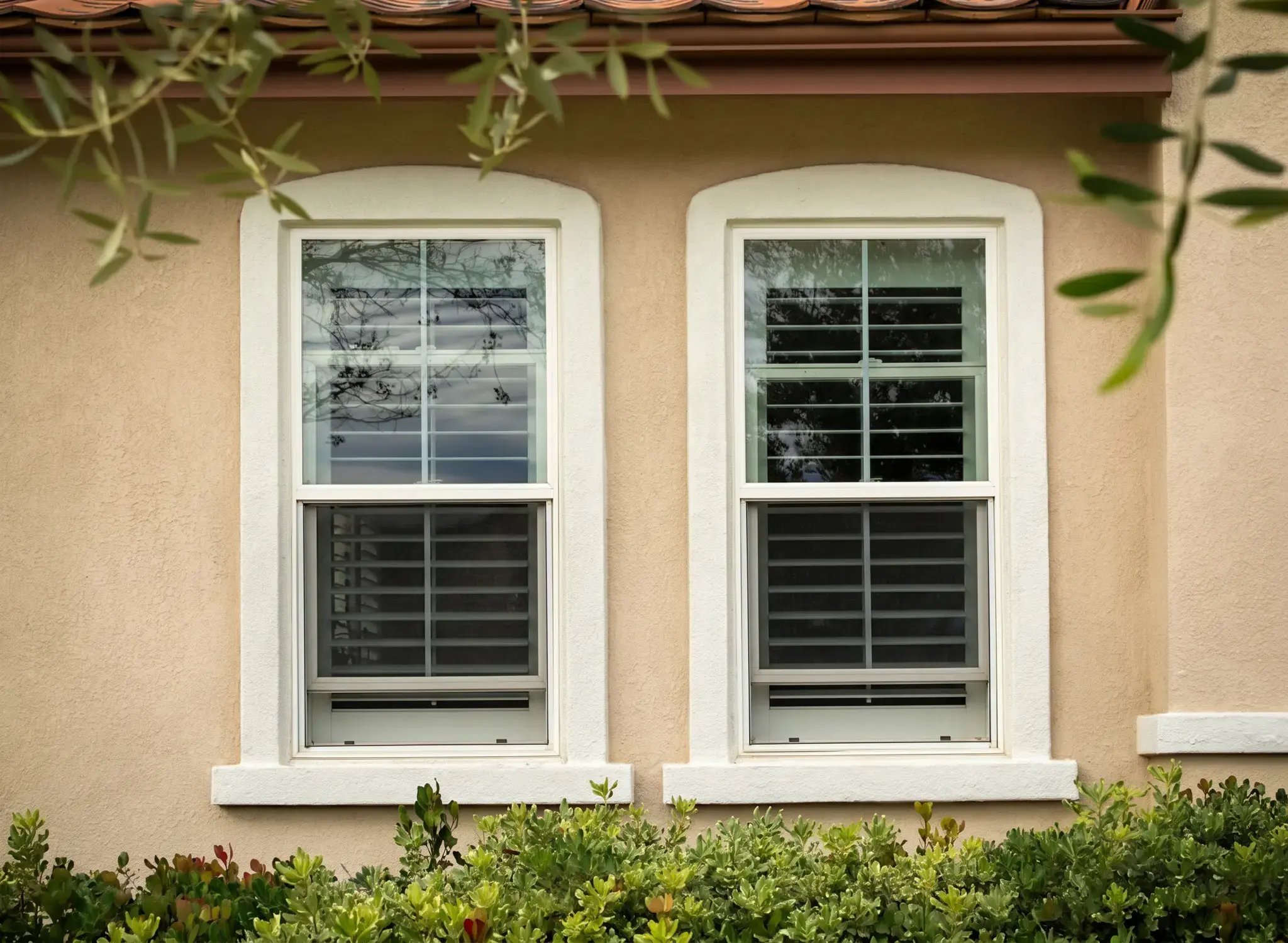Two white single-hung windows after replacement on a tan stucco single-family home