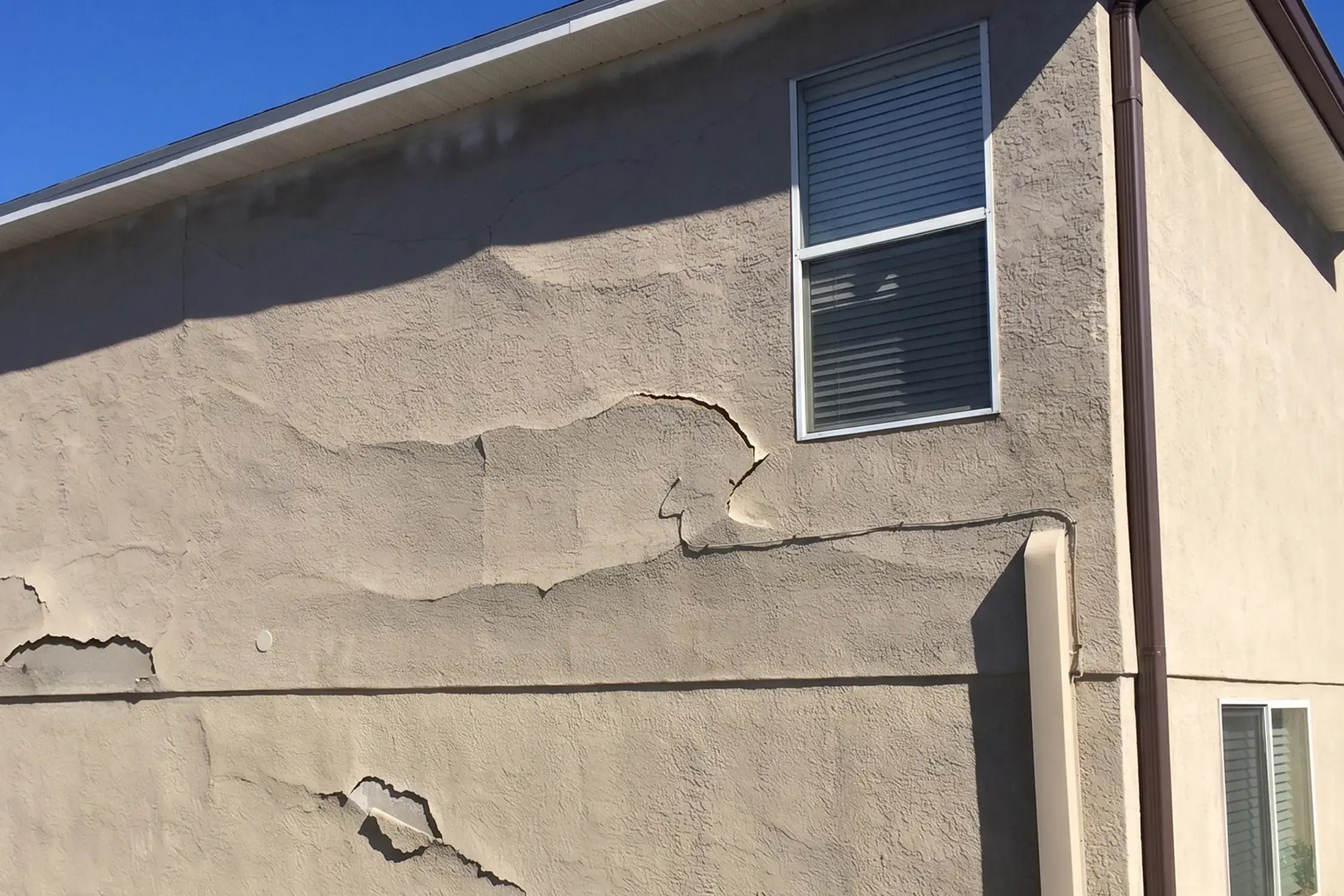 Large sections of stucco delaminating and cracking off a two-story home wall before exterior stucco repair