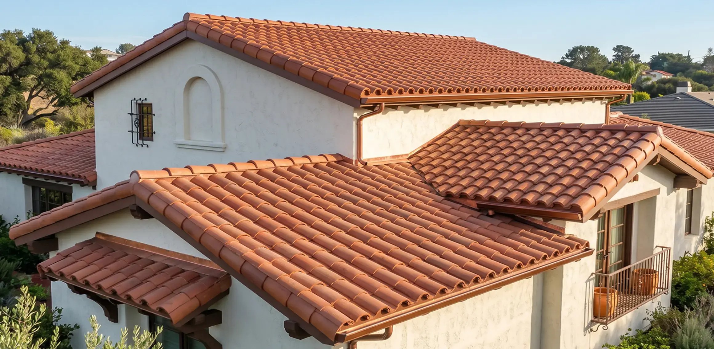 Two-piece clay barrel roof tiles on a white Spanish-style home with copper gutters and downspouts