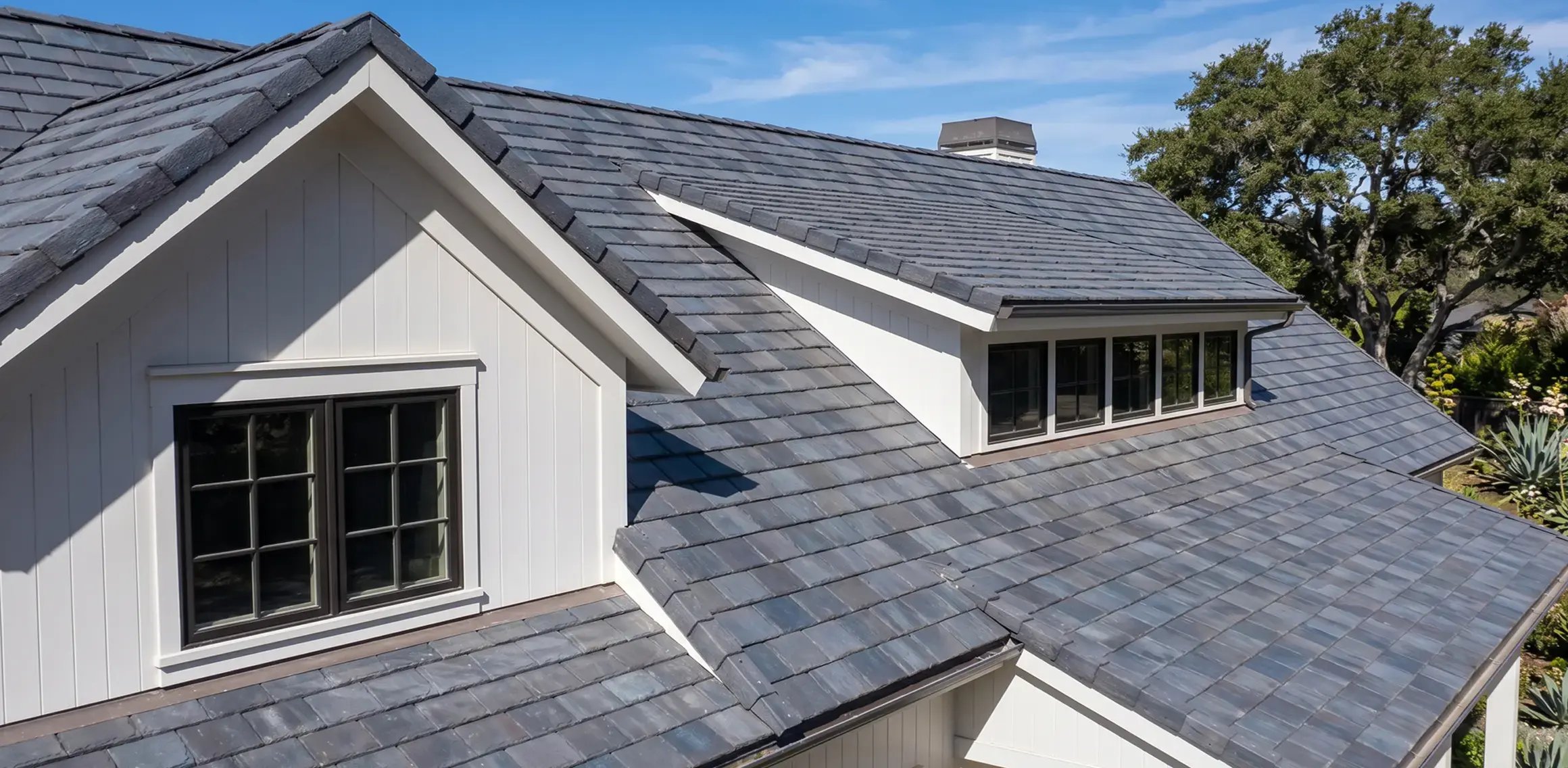 Dark composite slate-look roof tiles on a white farmhouse-style single-family home — Hybrid Renovations