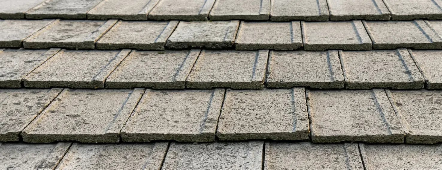 Flat low-profile concrete roof tiles in weathered gray, close-up showing the clean streamlined tile courses