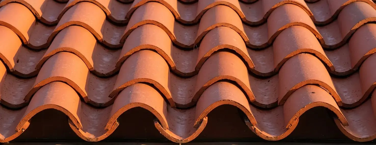 Two-piece mission barrel clay roof tiles in terracotta orange, close-up of the rounded cap-and-pan profile