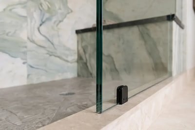 Frameless glass panel and black clamp meeting the low threshold after a tub-to-shower conversion