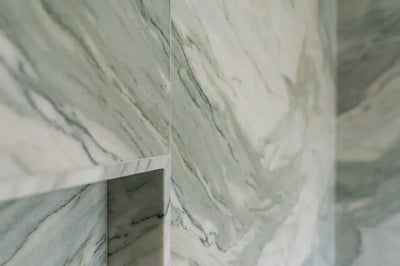 Green and white marble slab walls with a recessed niche return after a tub-to-shower conversion