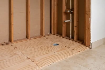 New plywood subfloor screwed down around the relocated shower drain before waterproofing