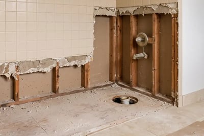 Alcove after bathtub removal with tile stripped to studs and the old drain opening exposed